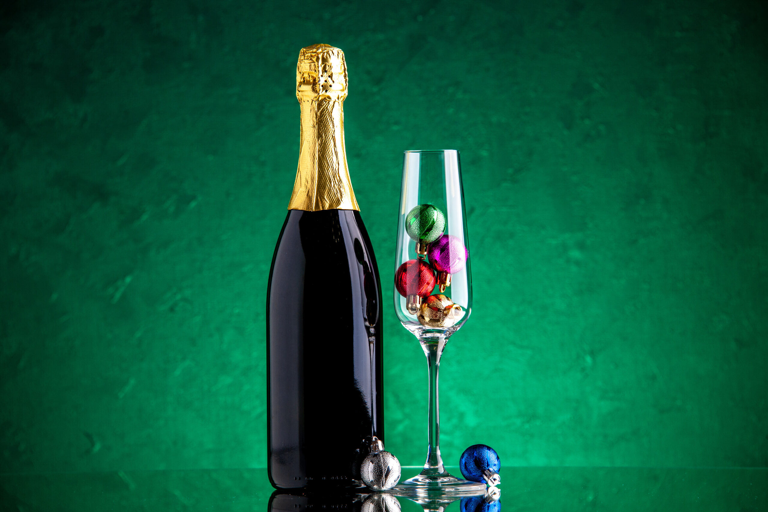 vue de face champagne petites boules de noel dans un verre a vin sur une surface verte scaled